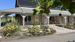 Ein Haus mit überdachter Veranda, Ziegelaußenwand und einem Garten mit verschiedenen Pflanzen und Blumen.