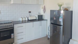 Ett modernt kök med vita skåp, ett kylskåp i rostfritt stål, en mikrovågsugn och en spis.