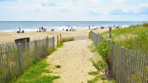 Une plage de sable bordée d’une clôture en bois et un sentier menant à l’eau.