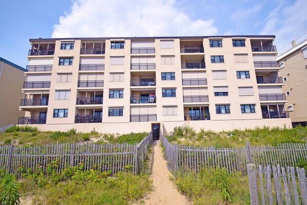 Un edificio residencial de varios pisos con balcones, una entrada central y una cerca alrededor.