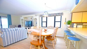 Un salon avec un canapé à rayures, une table à manger en bois avec des chaises, et un coin cuisine doté de tabourets de bar.