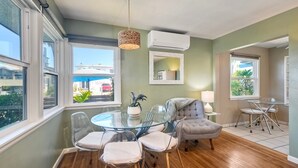 A dining area with a glass table, clear chairs, a grey armchair, and a hanging light fixture. - Walk 2 Beach, EV Charger, Outdoor Dining, 2 Units (Carlsbad)