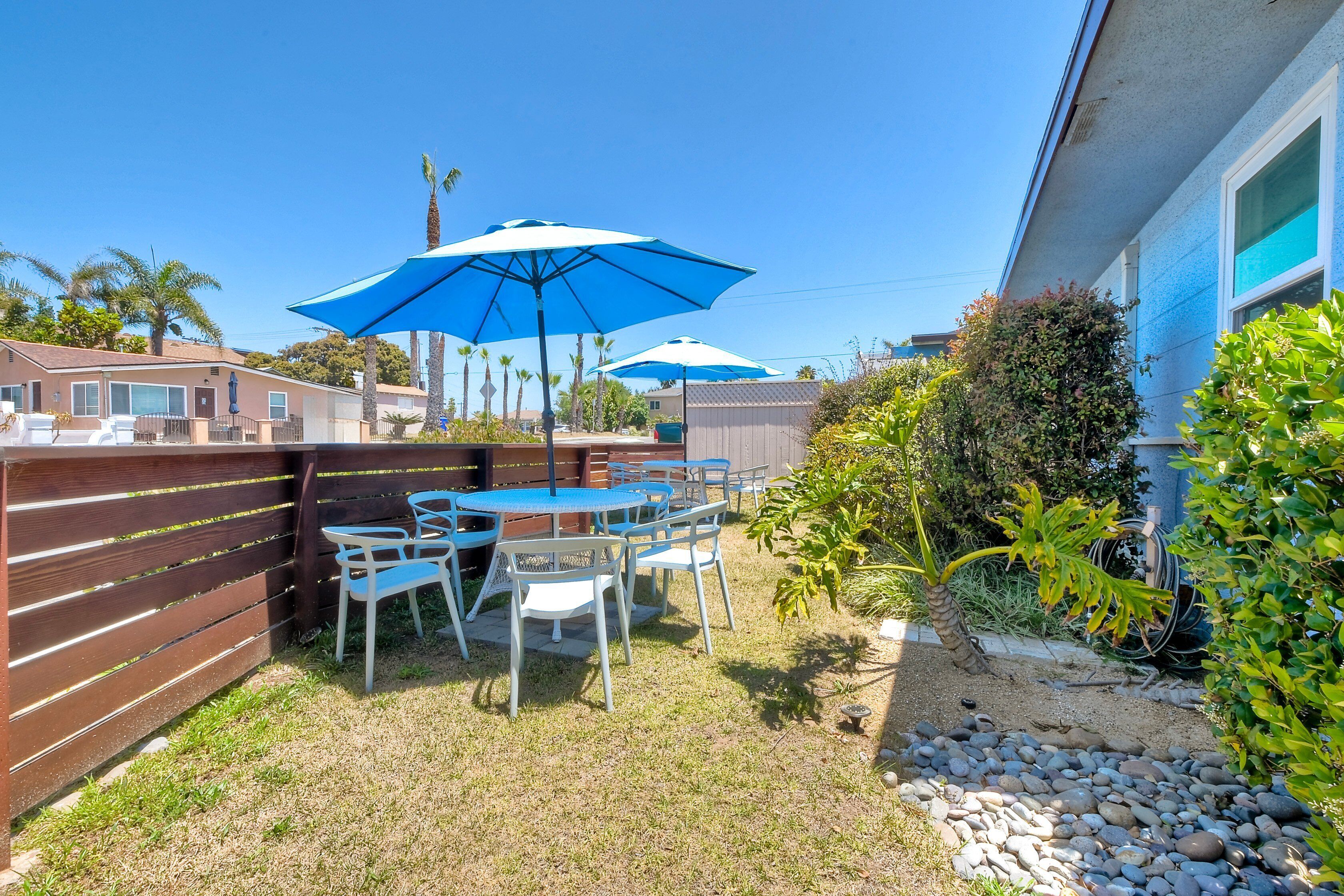 Een terras met een tafel en stoelen, twee blauwe parasols, en een houten omheining.