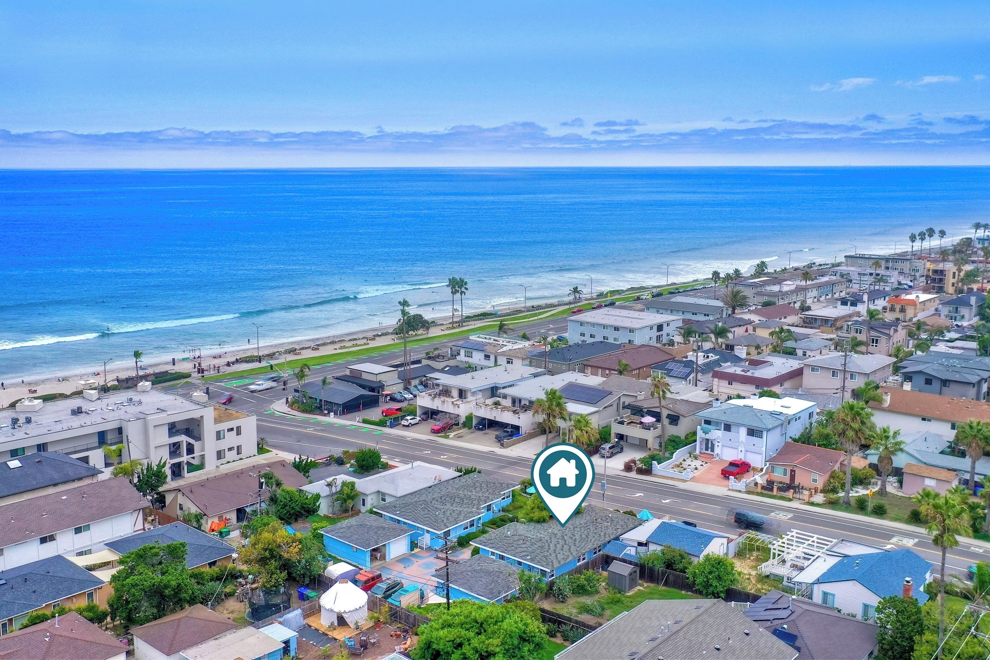 A coastal residential area with a mix of modern and traditional houses, a clear view of the ocean, and a road with a traffic sign.