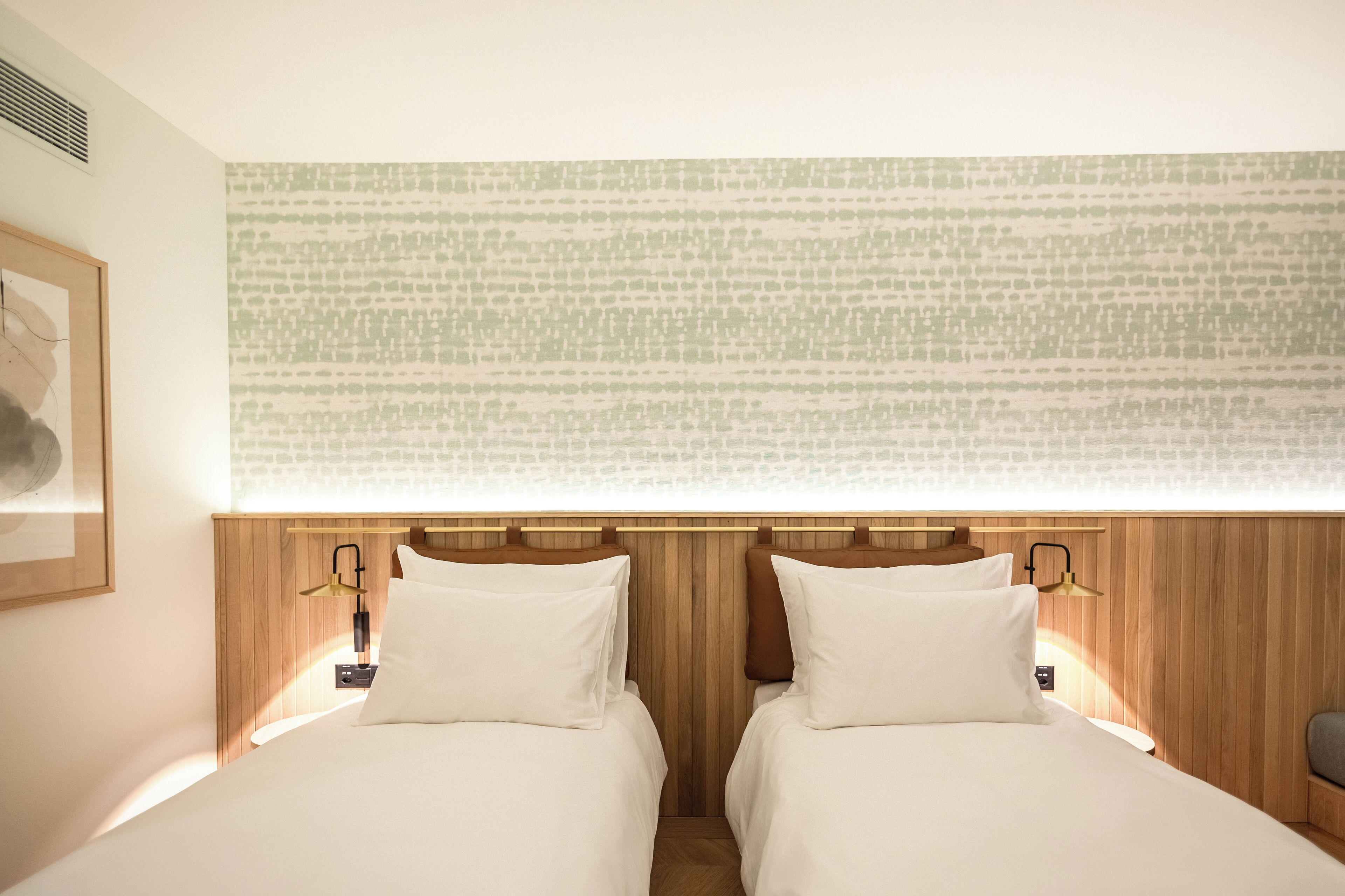 A hotel room with two beds, wooden headboards, and a patterned wall.
