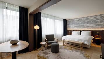 Una habitación de hotel moderna con una cama grande, una mesa redonda, una silla y una mesita auxiliar.