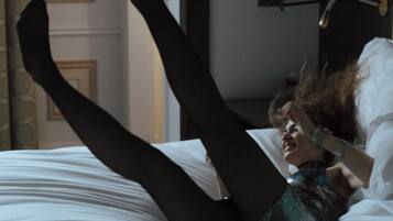 A person lying on a bed with their legs raised, a lamp, and a door in the background.