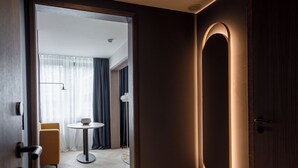 A modern hotel room with a wooden floor, a round table, and a door with a circular light feature.