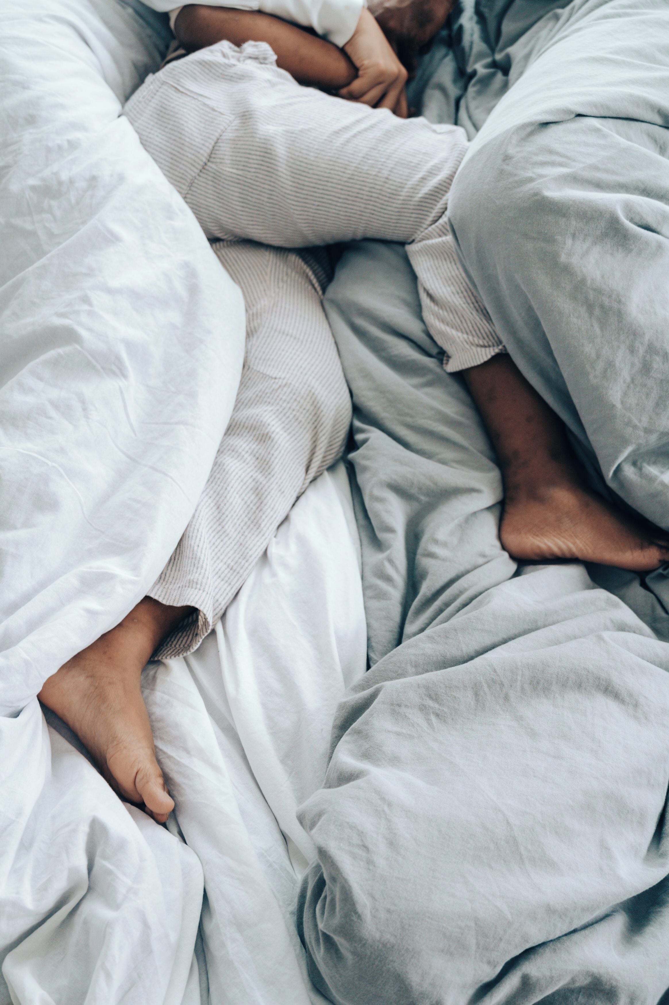 Una cama con ropa de cama blanca y gris, un almohadón a rayas y una persona acostada.