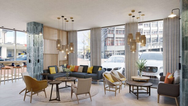 A modern hotel lobby with a sofa set, chairs, a coffee table, and large windows offering a view of the street.
