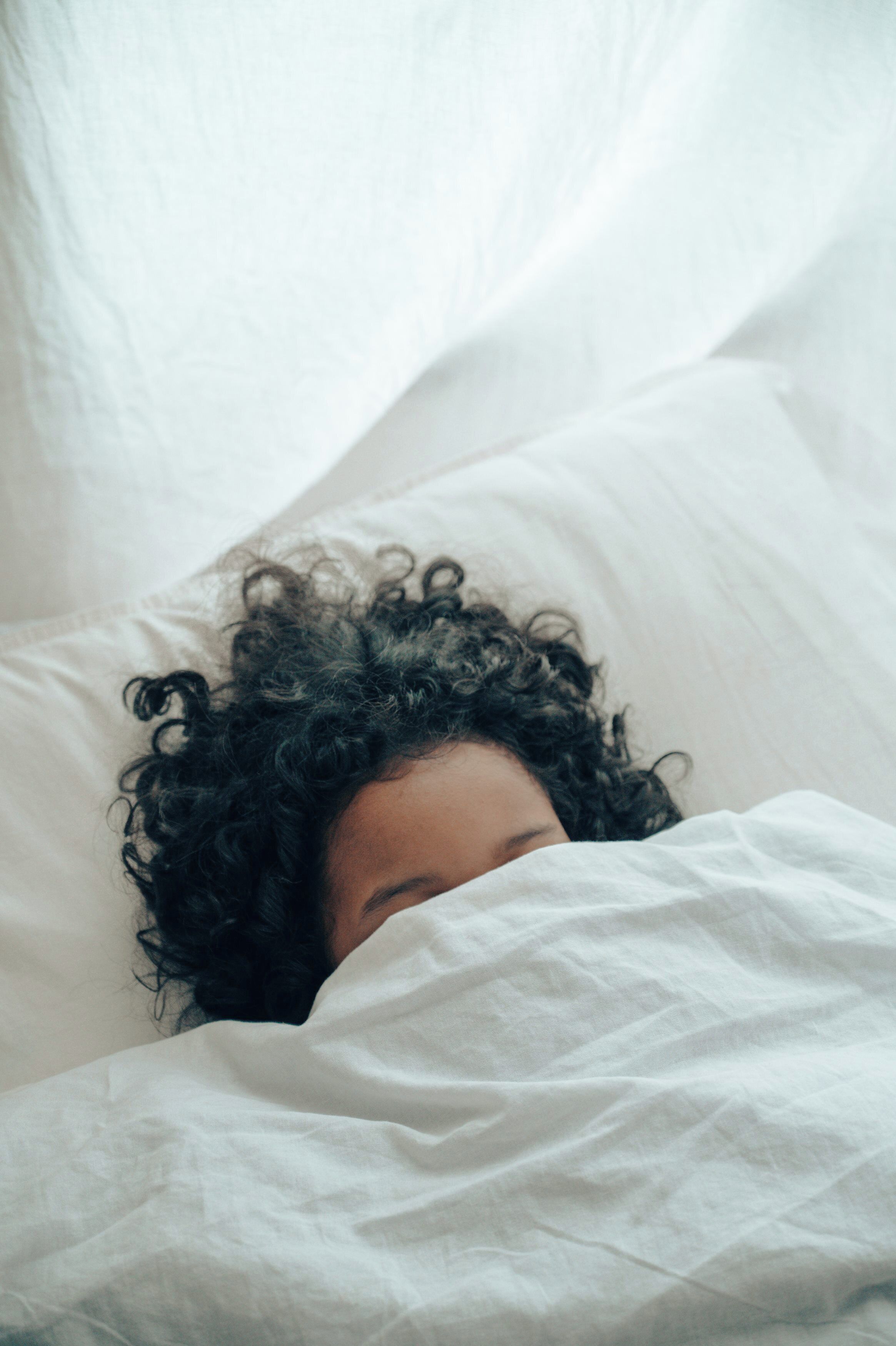 A person lying in bed with white bedding.