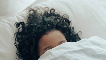 A person lying in bed with white bedding.