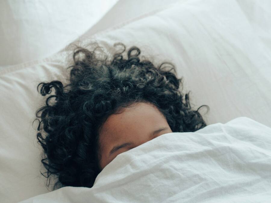 A person lying in bed with white bedding.