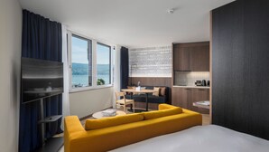 A modern hotel room with a bed, a yellow sofa, a dining area, and a kitchen.