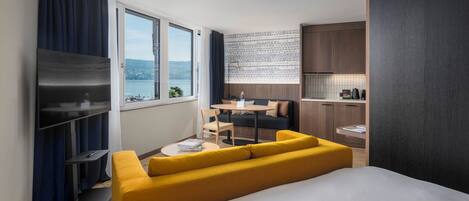 Una habitación de hotel moderna con una cama, un sofá amarillo, un comedor y una cocina.