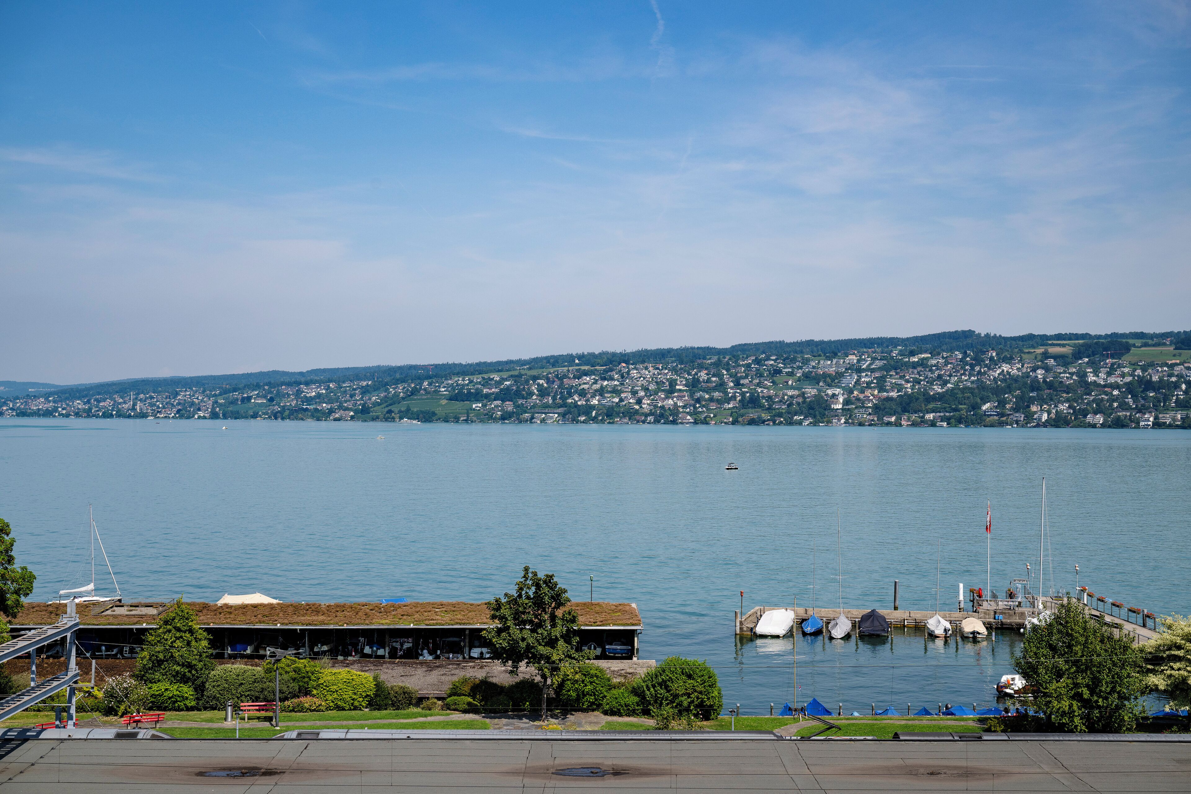 A waterfront view with a dock, boats, and a building with a green roof.