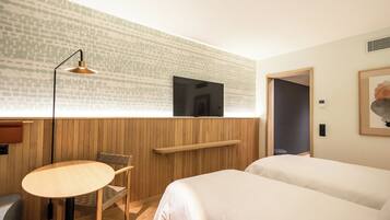 A hotel room with a wooden wall, a television mounted above a bed, a small round table, and a chair.