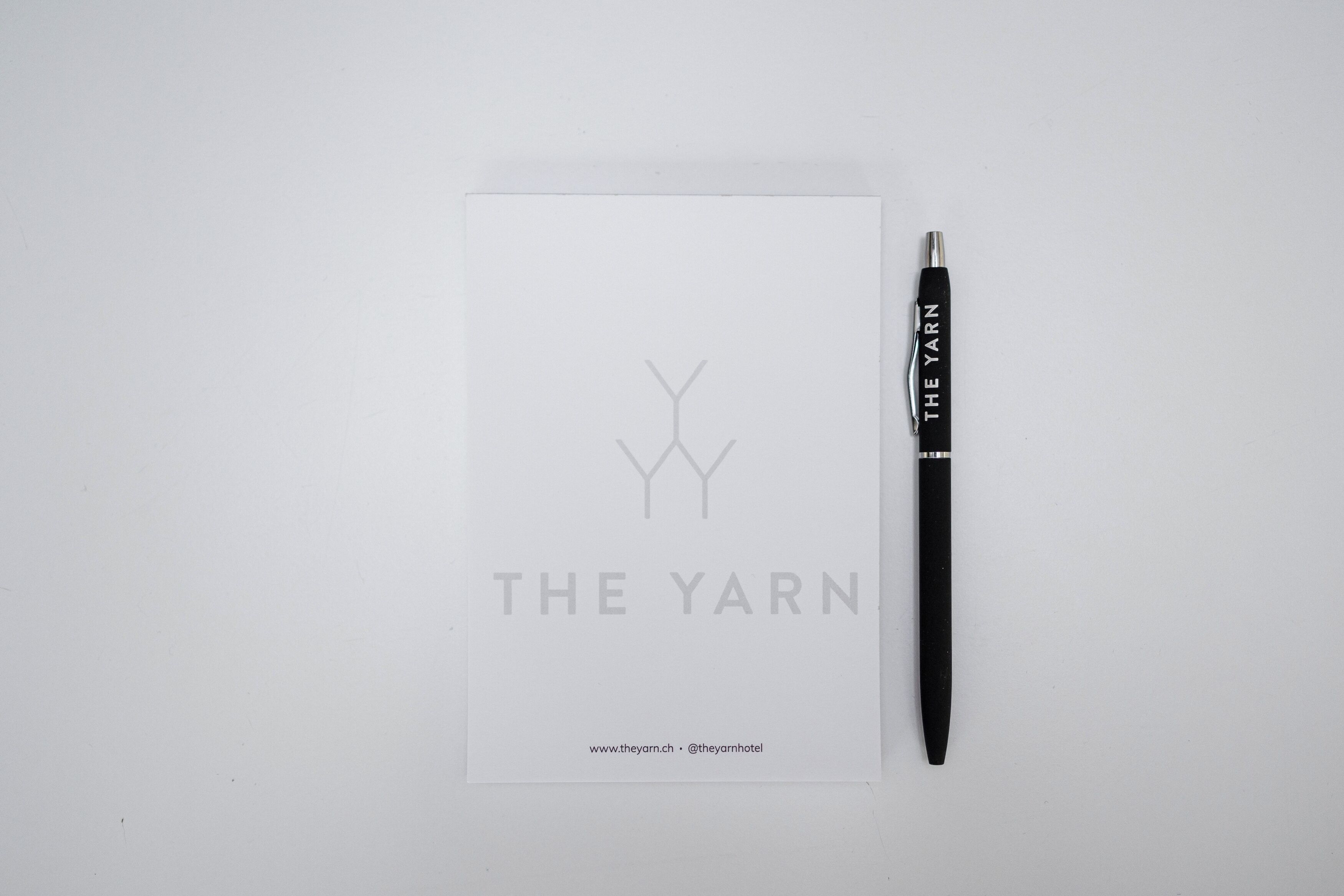 Ein weißes Blatt Papier mit dem Logo "THE YARN" und einem schwarzen Stift daneben.