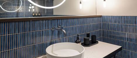 Une salle de bain moderne avec un grand miroir rond, un lavabo blanc et des murs recouverts de carreaux bleus.