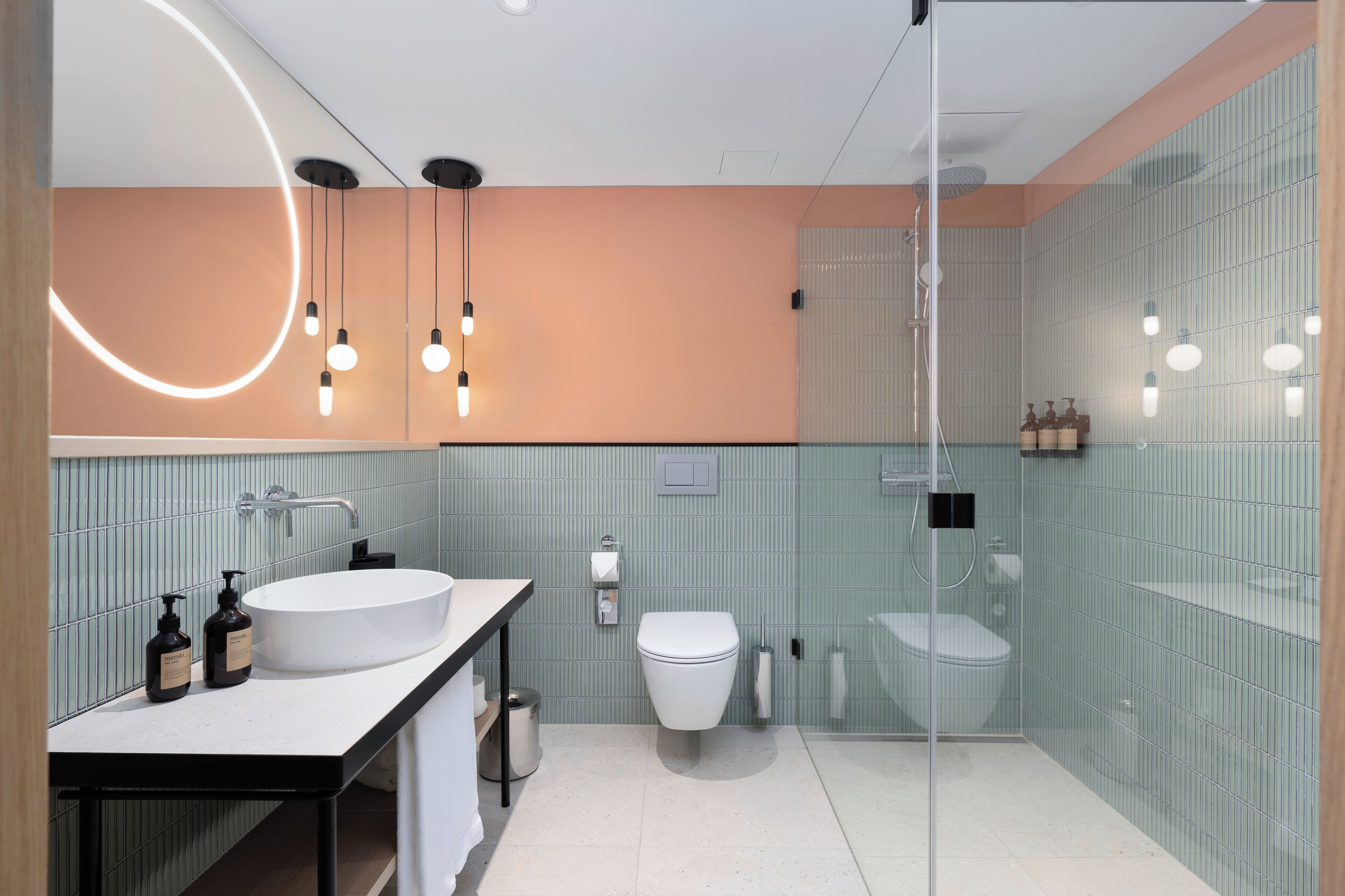 Un baño moderno con un lavamanos grande de color blanco, un inodoro y una zona de ducha con mampara de vidrio.