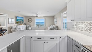 A spacious kitchen with white cabinetry, a large island, and a view to the ocean.