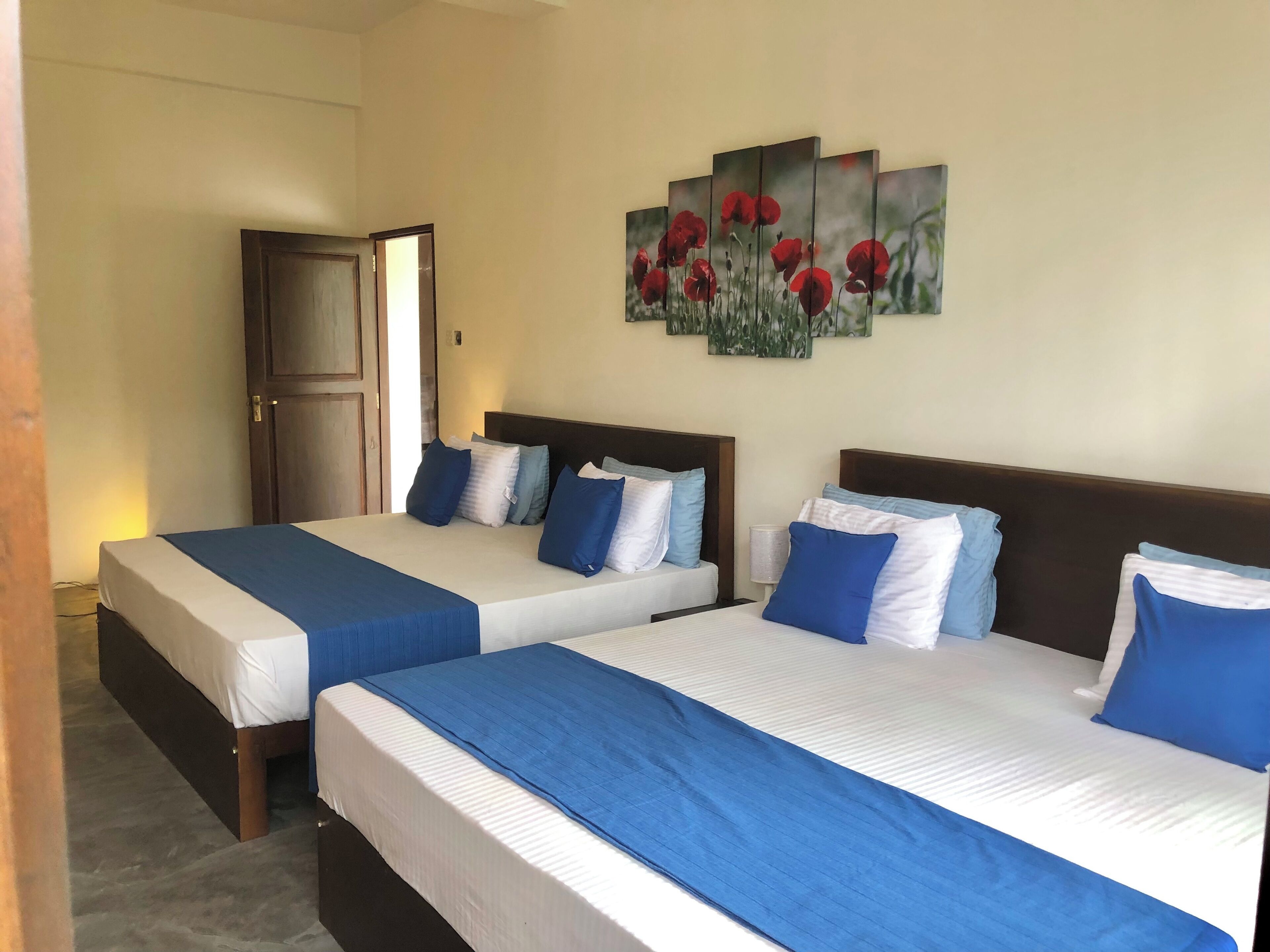 A hotel room with two beds, each with blue and white bedding, and a large painting of red flowers on the wall.