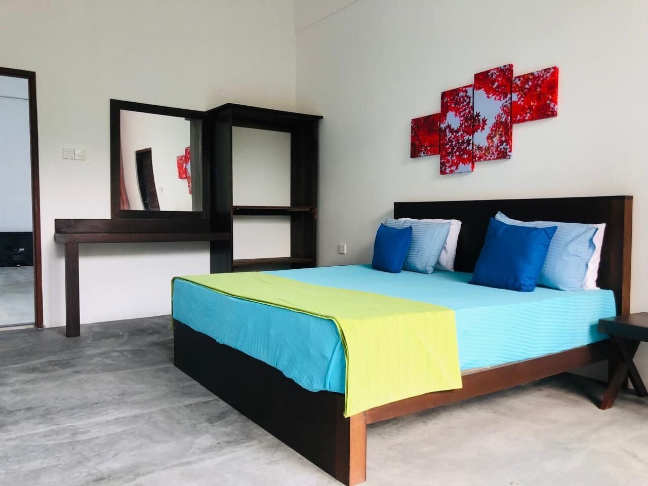 Un dormitorio con cama, mesita de noche, escritorio y un cuadro abstracto rojo en la pared.