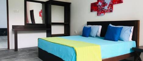 A bedroom with a bed, a nightstand, a desk, and a red abstract painting on the wall.