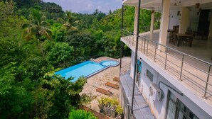 A pool with a surrounding deck, a balcony with outdoor seating, and lush greenery in the background. - Red Letter Hotel (Kandy)