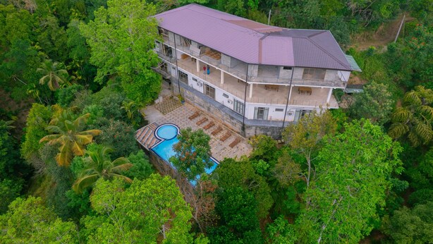 A multi-story house surrounded by dense greenery, with a swimming pool on the ground floor. - Red Letter Hotel (Kandy)