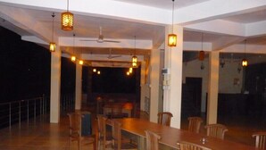 A spacious dining area with a long wooden table and chairs, pendant lighting, and a ceiling fan. - Red Letter Hotel (Kandy)
