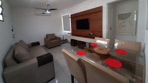 Un salon moderne avec un canapé, une table à manger agrémentée de sets de table rouges, un téléviseur fixé au mur et un ventilateur de plafond.