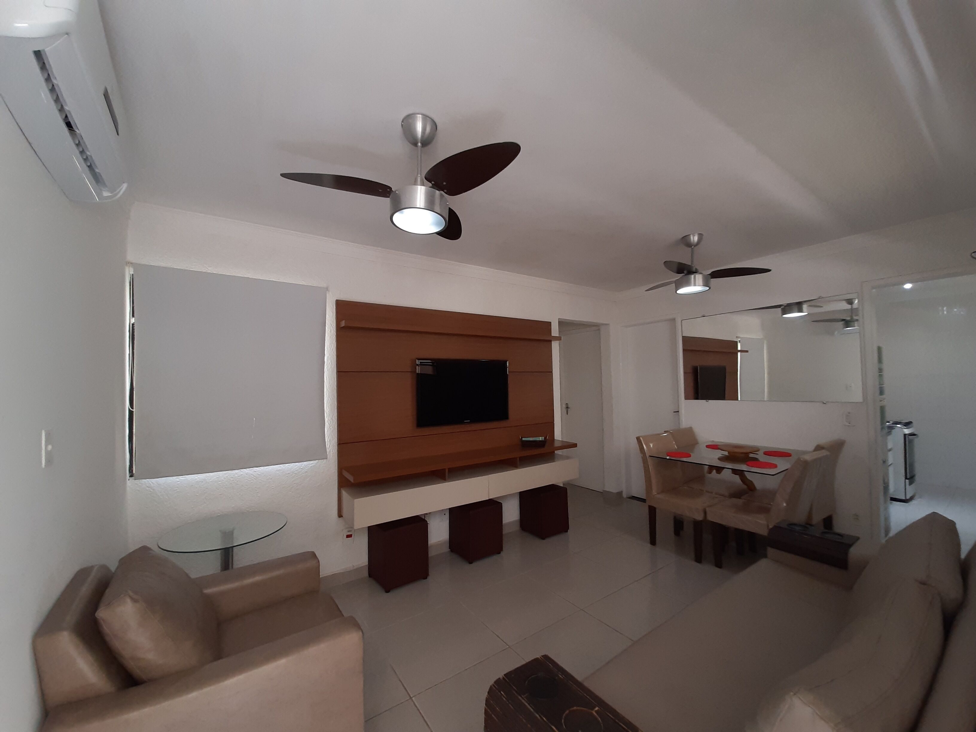 Een moderne woonkamer met een flatscreen televisie, plafondventilatoren, een eethoek met tafel en stoelen, en een bank.