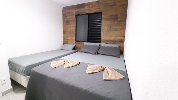 Une petite chambre moderne avec deux lits simples, une tête de lit en bois et une fenêtre équipée de stores.