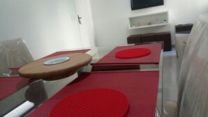 Un espace repas moderne avec des tables en verre et des sets de table rouges, un meuble blanc et un téléviseur fixé au mur.