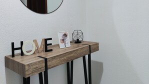 Una consola de madera con la palabra "HAVE" escrita, un espejo redondo encima y una lámpara fijada a la pared.