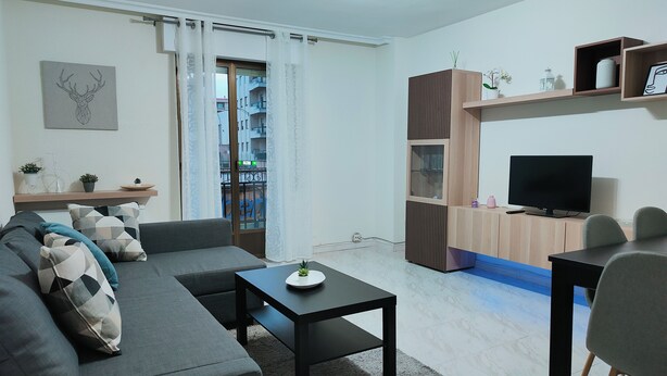Una sala de estar moderna con un sofá gris, una mesa de centro, un televisor y un comedor con mesa y sillas.