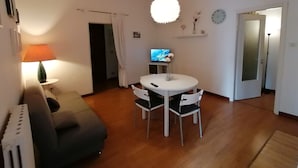 A cozy living room with a sofa, a round dining table with chairs, a TV, and a lamp.