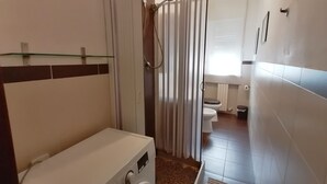 A compact bathroom with a washing machine, a toilet, and a shower area.