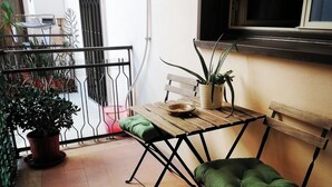 A balcony with a wooden table and a green cushioned chair, a potted plant, and a metal railing.
