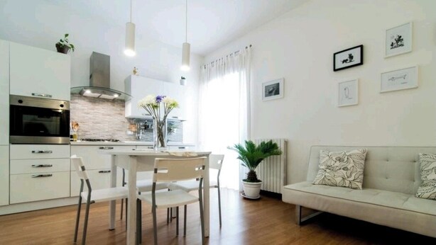 A modern kitchen with white cabinets, a stainless steel oven, and a dining area with a white table and chairs.