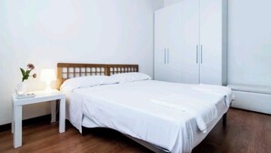 A bedroom with a bed, a nightstand, a wardrobe, and a bedside table with a lamp and a flower.