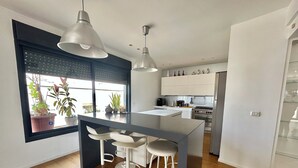 A modern kitchen with a central island, bar stools, pendant lighting, and a view of the outdoors through a window. - Beautiful 2BR In Ramat Gan (Ramat Gan)