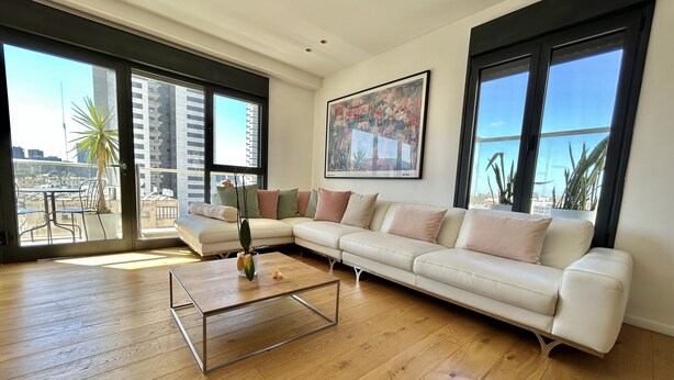 A spacious living room with a large sectional sofa, a coffee table, and large windows offering a city view. - Beautiful 2BR In Ramat Gan (Ramat Gan)