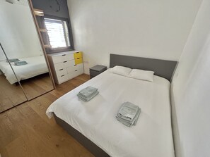 Une chambre à coucher avec un lit, une table de chevet, un miroir, une commode et une fenêtre.