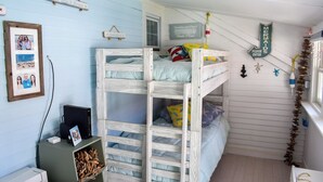Une chambre avec un lit superposé, un mur bleu, un bureau avec un ordinateur et une étagère remplie de livres.