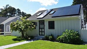 Une maison avec des panneaux solaires sur le toit, une porte d’entrée et un petit porche.