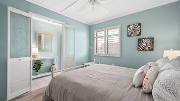 A bedroom with a bed, a dresser, a vanity with a mirror, and a ceiling fan.