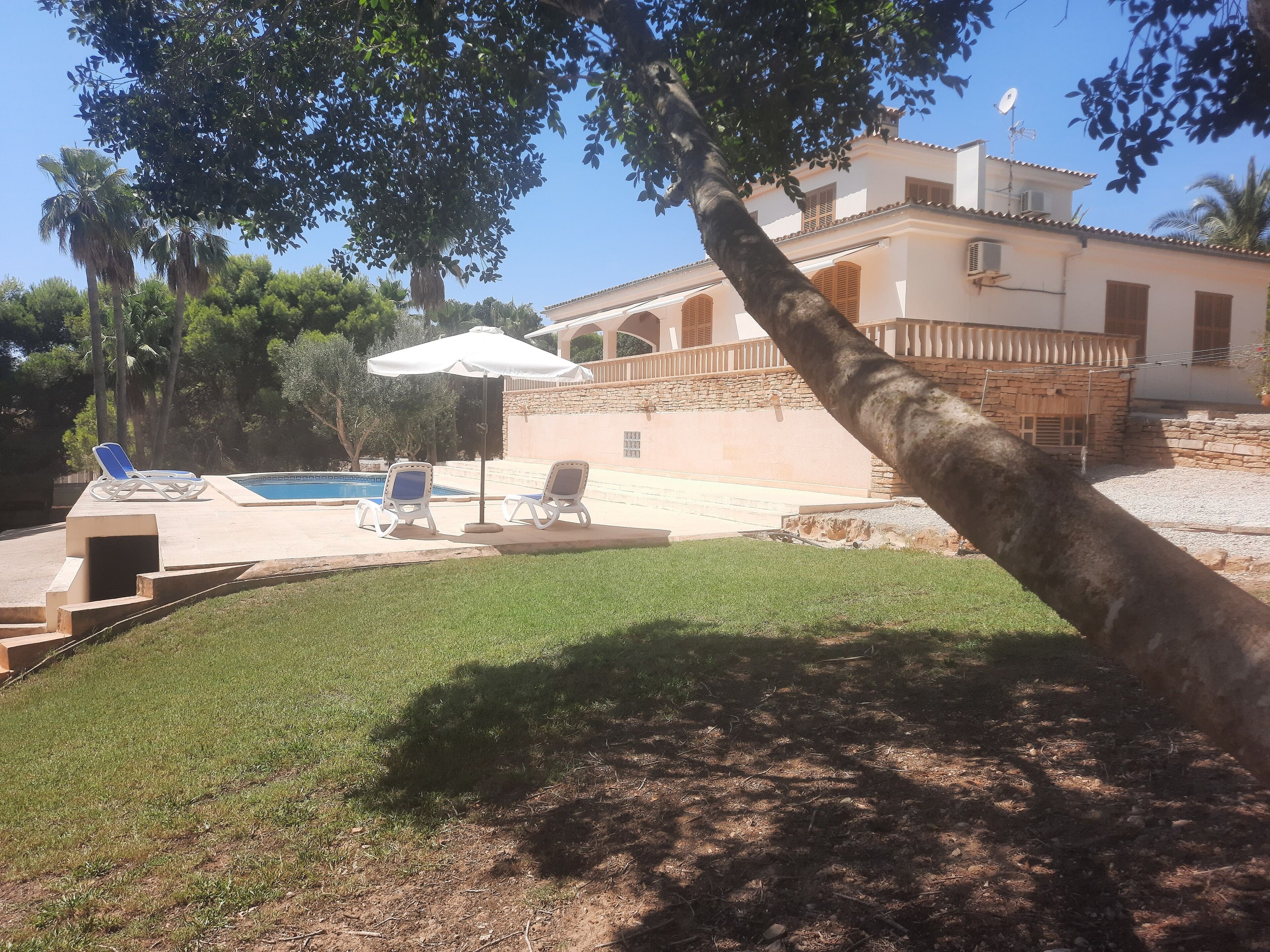 Un espace piscine agrémenté de chaises longues et d’un parasol blanc, entouré d’une pelouse bien entretenue et d’un bâtiment en pierre doté d’un toit en tuiles.