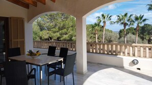 Une terrasse extérieure avec une table et des chaises, un plafond en bois et une vue sur des palmiers et une végétation luxuriante.